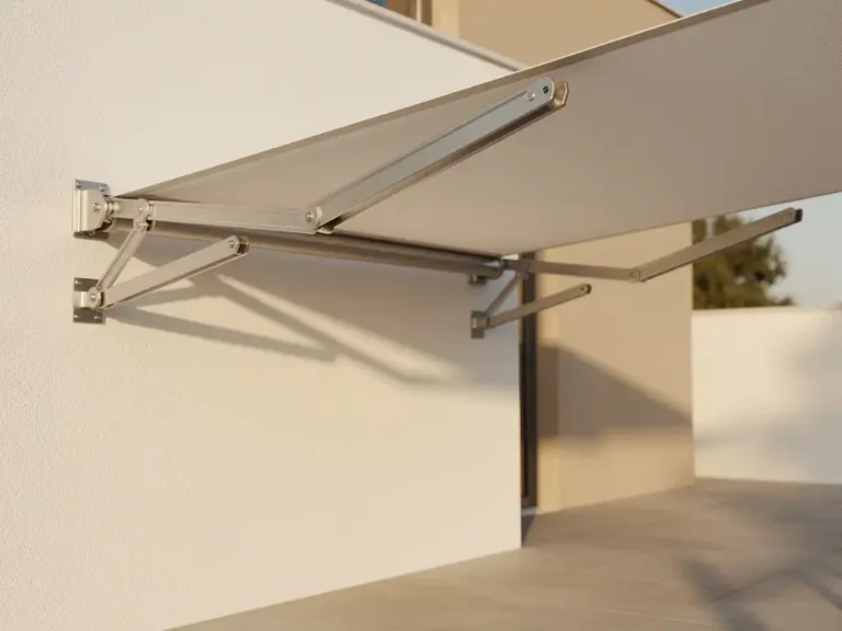 Uitgeschoven knikarmschermen bevestigd aan witte gevel boven zonnig terras, met zichtbare scharnieren en strak gespannen doek.