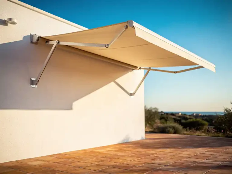 Moderne uitschuifbare zonneluifel met zichtbare schaararmen aan witte gevel, uitgestrekt over terras met terracotta tegels onder blauwe lucht.